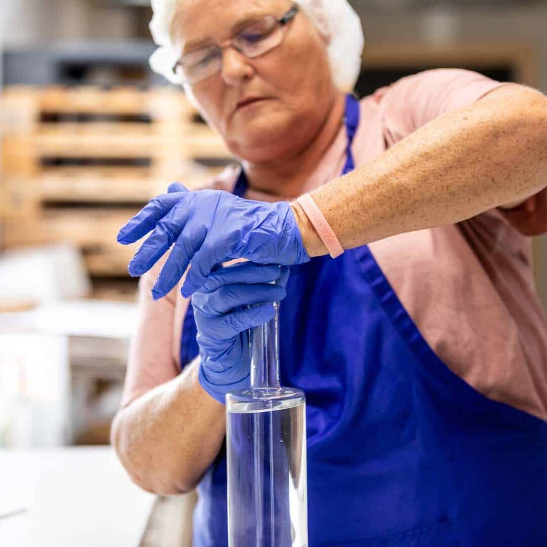 A woman wearing gloves and a hairnet sealing a bottle of vodka